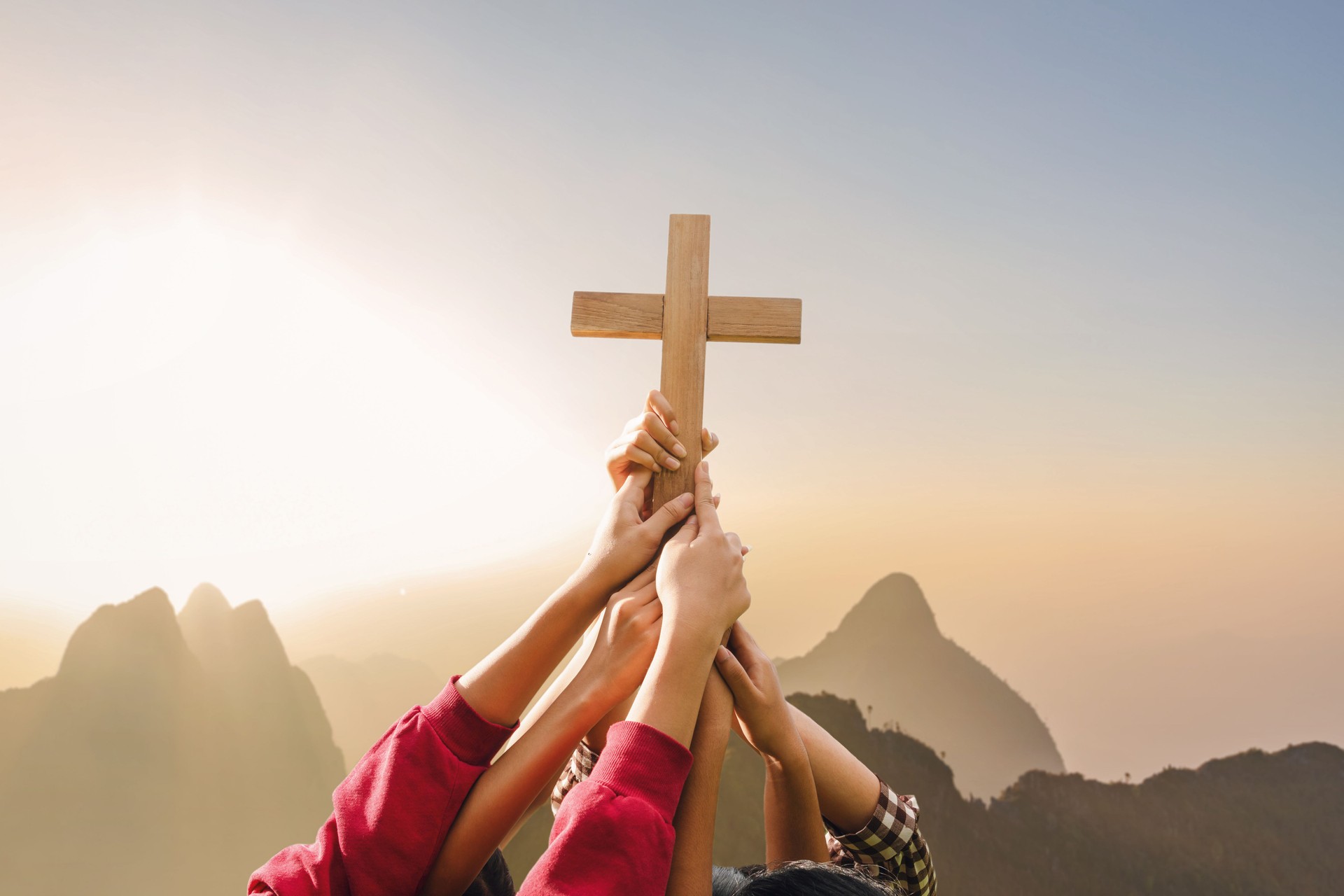 Friendship hands praying and holding Christian cross for worshipping God on mountain at sunrise background. Christian, Christianity, Religion copy space background. Easter Sunday concept: